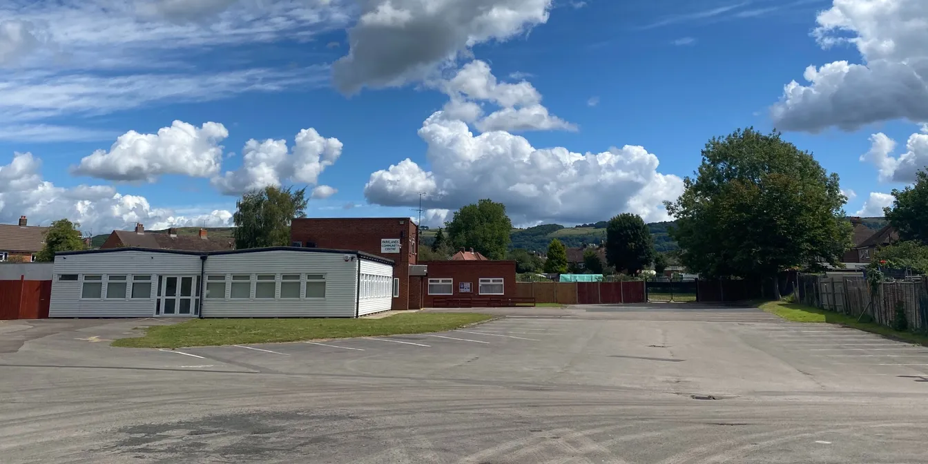 Parklands Community Centre and its car park under a blue sky, with hills in the distance.